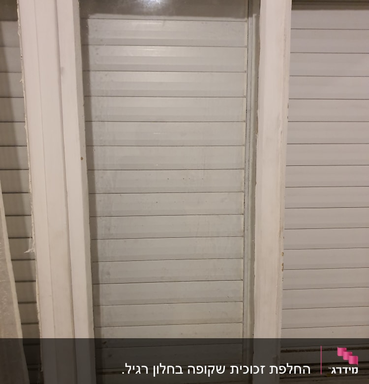 חלון זכוכית עם מסגרת לבנה ותריסים סגורים